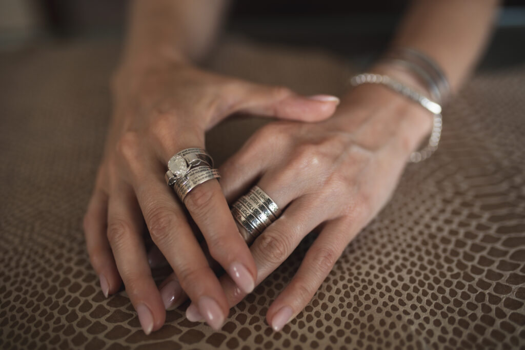 Hands wearing multiple sterling silver rings engraved with Hebrew blessings and verses