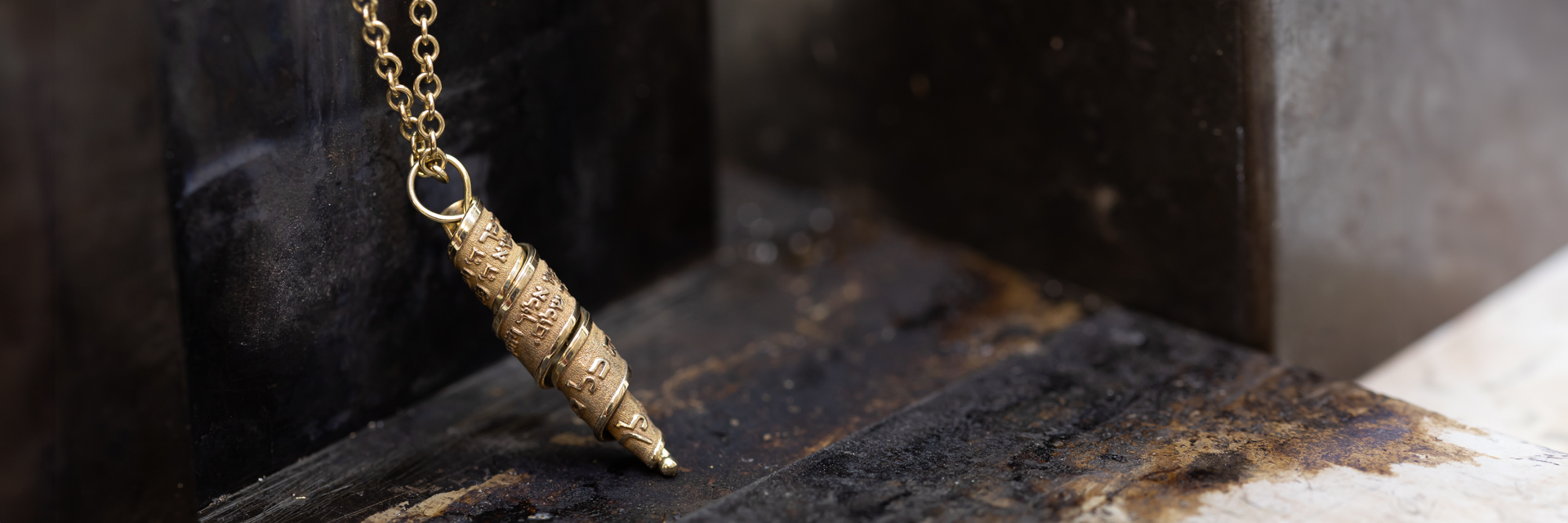 Close-up of a handmade gold Judaica necklace with Hebrew engraving