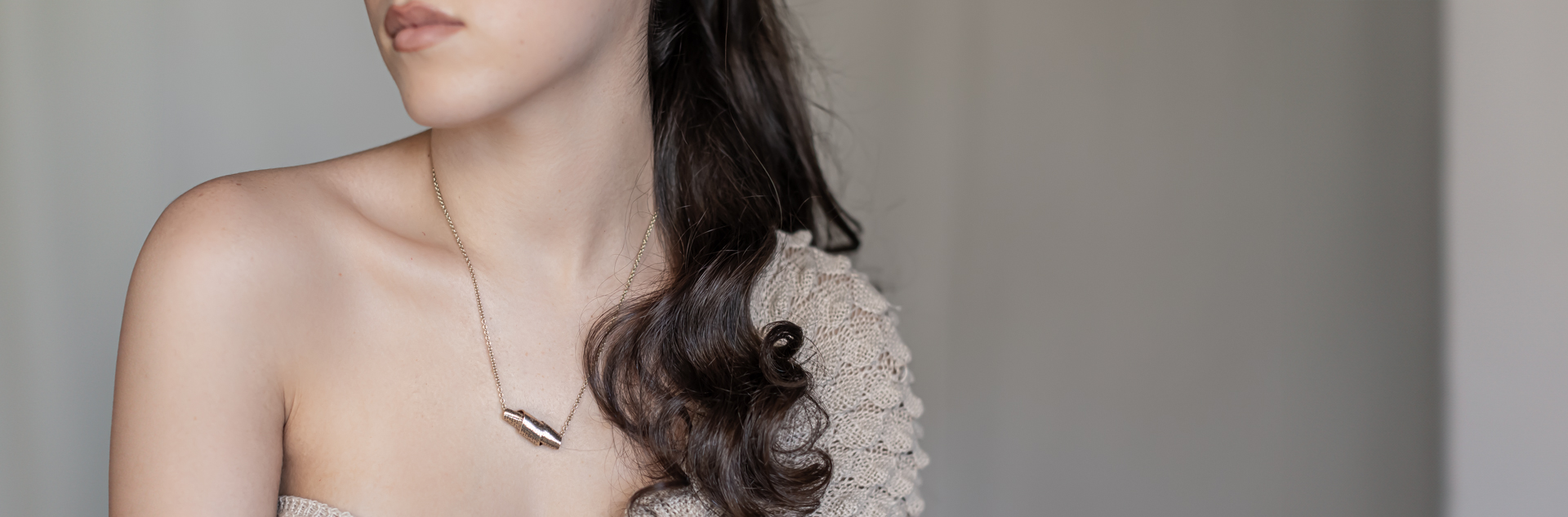 Woman wearing a gold scroll necklace with Hebrew engraving on a neutral background