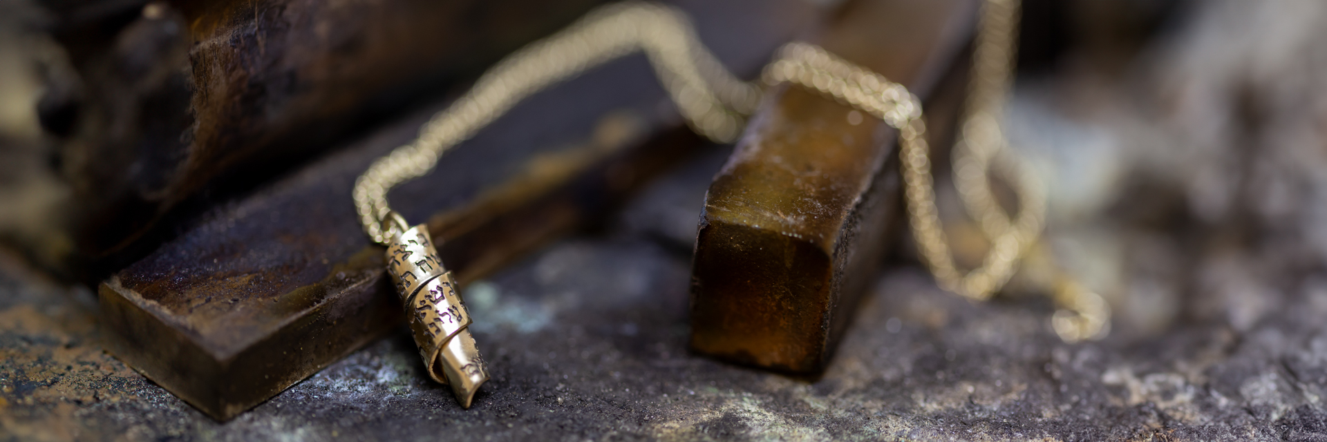 Gold scroll necklace with personalized Hebrew engraving on rustic metal background