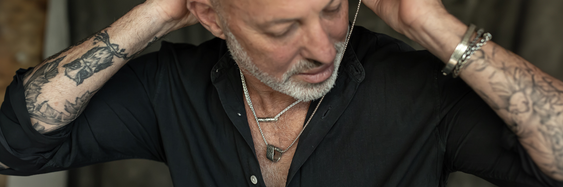 Tattooed man wearing layered silver Hebrew necklaces and bracelets